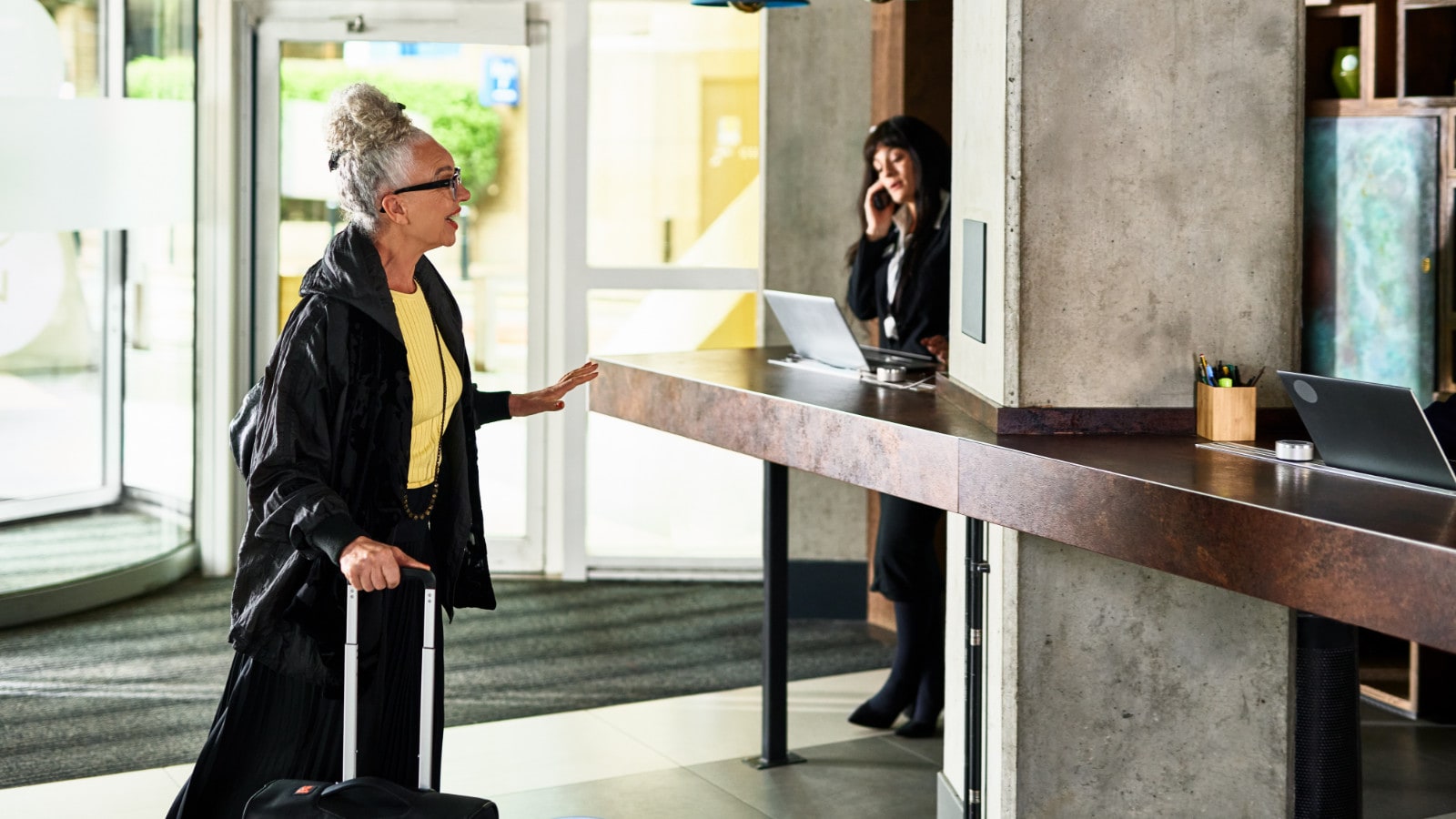 Woman in front of hotel reception desk talking and gesturing, hospitality industry, customer, service, hotel guest